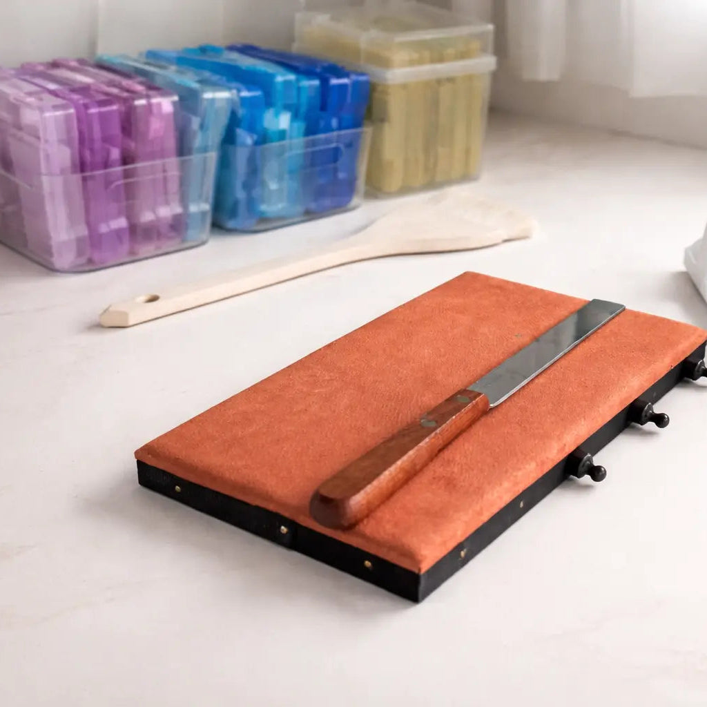 Gold leaf tools and materials arranged on a white studio desk, including a gilding cushion, knife,  and storage cases used in hand-finished original artworks.