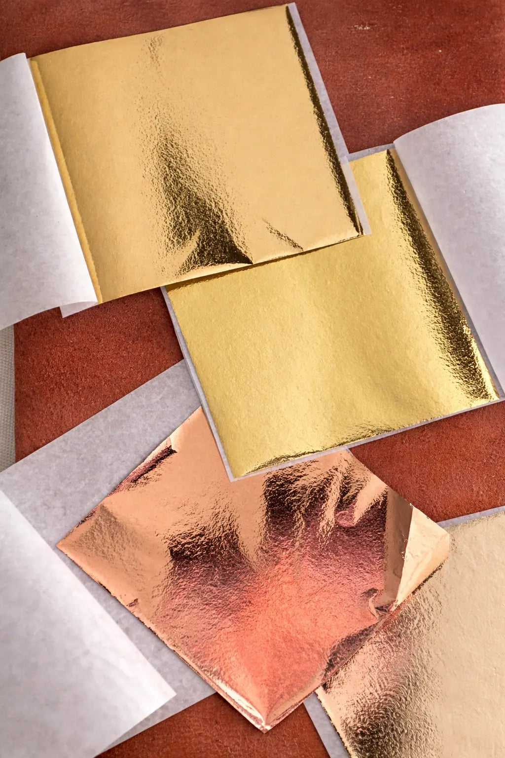 Sheets of gold and rose-gold leaf resting on a leather gilding pad, showing delicate texture and reflective surface.