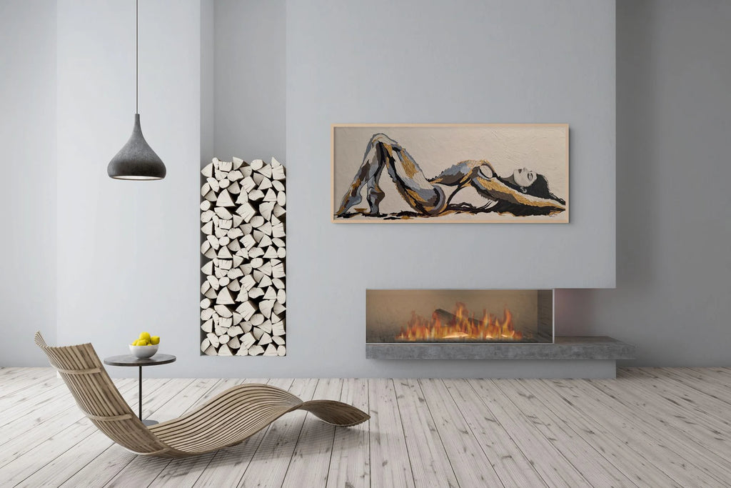 The Recline mixed media figurative painting with 23K gold leaf displayed in a modern neutral interior with oak frame.  The framed abstract painting of a reclining figure is on the wall above a linear fireplace. The room has light grey walls, a wood floor, a curved woven lounge chair, a small side table with lemons, and a decorative stack of white logs.