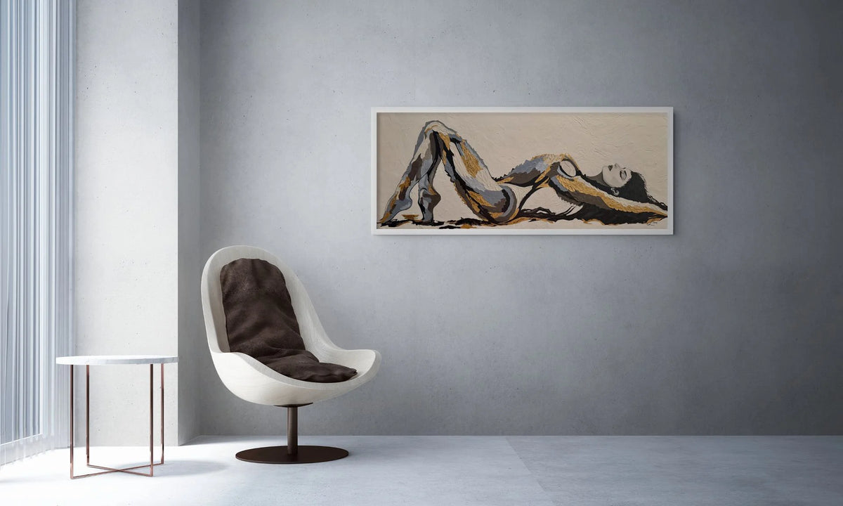 The Recline original figurative artwork with 23K gold leaf displayed in a contemporary interior with white frame in a horizontal orientation.  The art is depicting an abstract reclining female figure in beige, brown, and black tones, displayed on a textured grey wall in a modern minimalist room with a white swivel chair and a small side table.